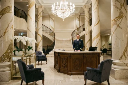Hall d'entrée luxueux d'un grand hôtel 5 étoiles avec colonnes en marbre, lustre en cristal et concierge en uniforme marine